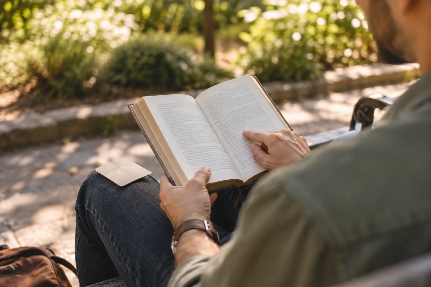 Una persona adulta comprueba un libro abierto junto a una tarjeta en un banco del parque.